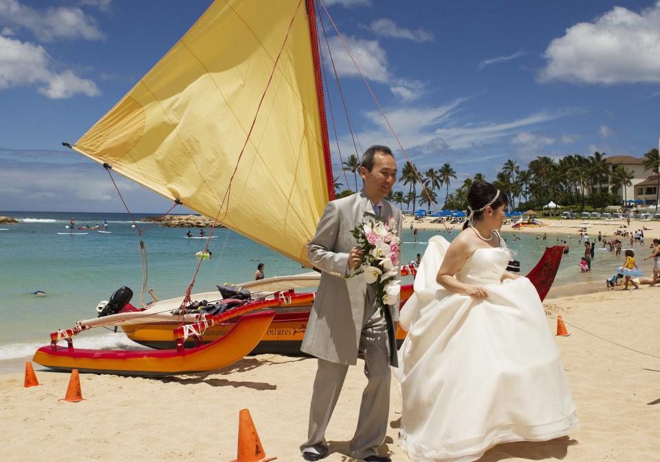 A Japanese couple walks past a sailing canoe on the beach after taking wedding pictures as two hurricanes approach the Hawaiian islands, in Honolulu, Hawaii, August 6, 2014. Hawaiians braced for a one-two punch from a pair of major storms headed their way on Wednesday, as Hurricane Iselle bore down on the islands packing high winds and heavy surf and Julio, tracking right behind, was upgraded to hurricane status. REUTERS/Hugh Gentry (UNITED STATES - Tags: ENVIRONMENT DISASTER SOCIETY)
