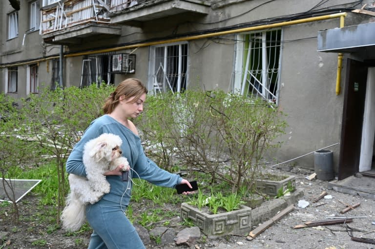 Una mujer camina con un perro en brazos junto a un edificio alcanzado por los misiles en el centro de la ciudad ucraniana de Járkov el 7 de abril de 2024 (Sergey Bobok)