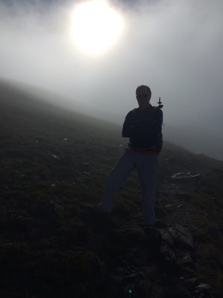 A shadowy image of a man standing on a mountain slope with the sun behind him