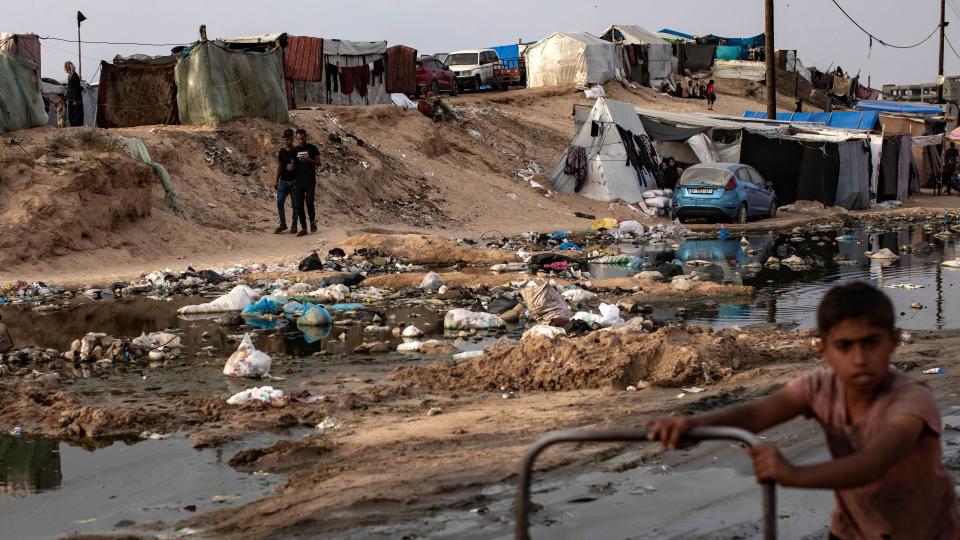 Un niño empuja un carro en una zona inundada y llena de basura en Rafah.