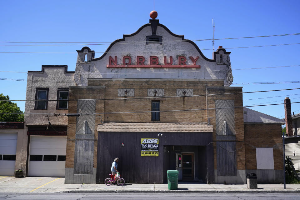 A man walks past a theatre that has been repurposed as a taxi service in Ellenville, N.Y., Wednesday, June 16, 2021. Less than 100 miles north of New York City, Ulster County is popular destination for weekenders headed to Woodstock or the Catskill Mountains. Though pretty, there are pockets of poverty. The county is working with the Center for Guaranteed Income Research at the University of Pennsylvania on a pilot program funded by private donations. One hundred households making less than $46,900 a year in May began receiving a $500 payment each month for a year. Recipients of the money can spend it as they wish, but will be asked to participate in periodic surveys about their physical health, mental health and employment status. (AP Photo/Seth Wenig)