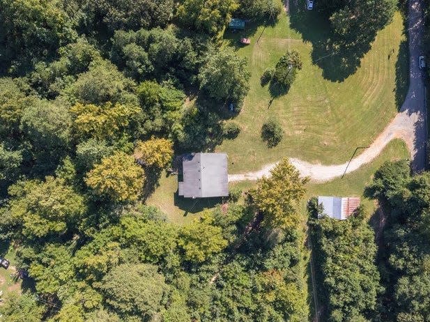 overhead shot of a home on a property, surrounded by trees and with a dirt winding driveway