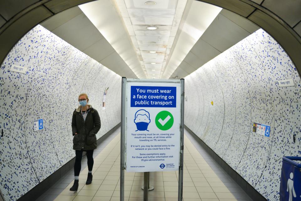  A woman wearing a face mask walks through the London Underground with a sign encouraging the public to use face-coverings at Green Park.