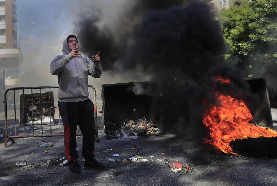 A protester shouts slogans in front of burning tires and garbage containers set on fire to block a main road during a protest against the increase in prices of consumer goods and the crash of the local currency, in Beirut, Lebanon, Tuesday, March 16, 2021. Scattered protests broke out on Tuesday in different parts of the country after the Lebanese pound hit a new record low against the dollar on the black market. (AP Photo/Hussein Malla)