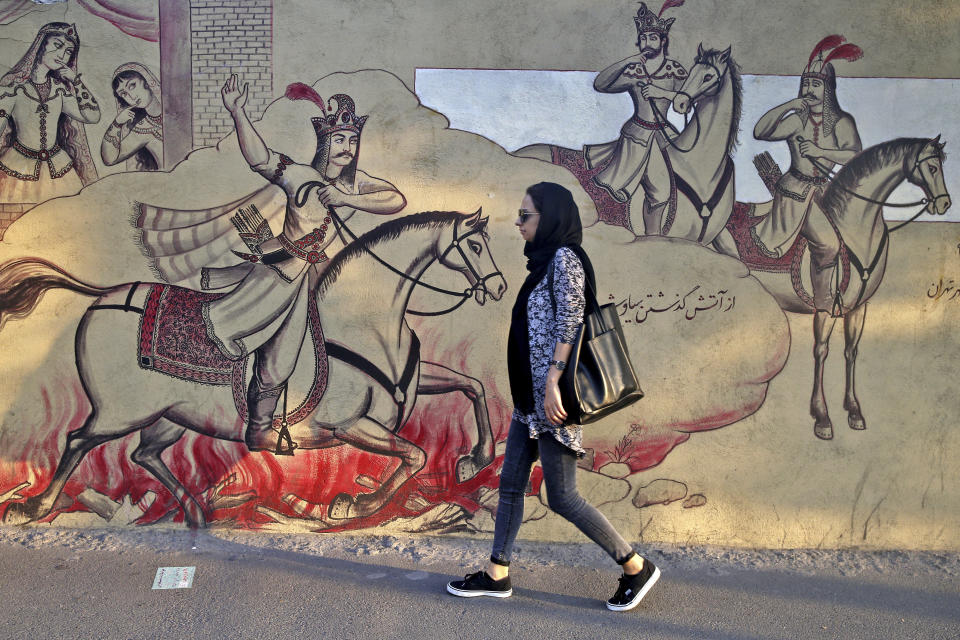 An Iranian woman walks past paintings of a Persian poetry in downtown Tehran, Iran, Monday, July 30, 2018. Iran's currency has dropped to a record low ahead of the imposition of renewed American sanctions, with many fearing prolonged economic suffering or possible civil unrest. (AP Photo/Ebrahim Noroozi)