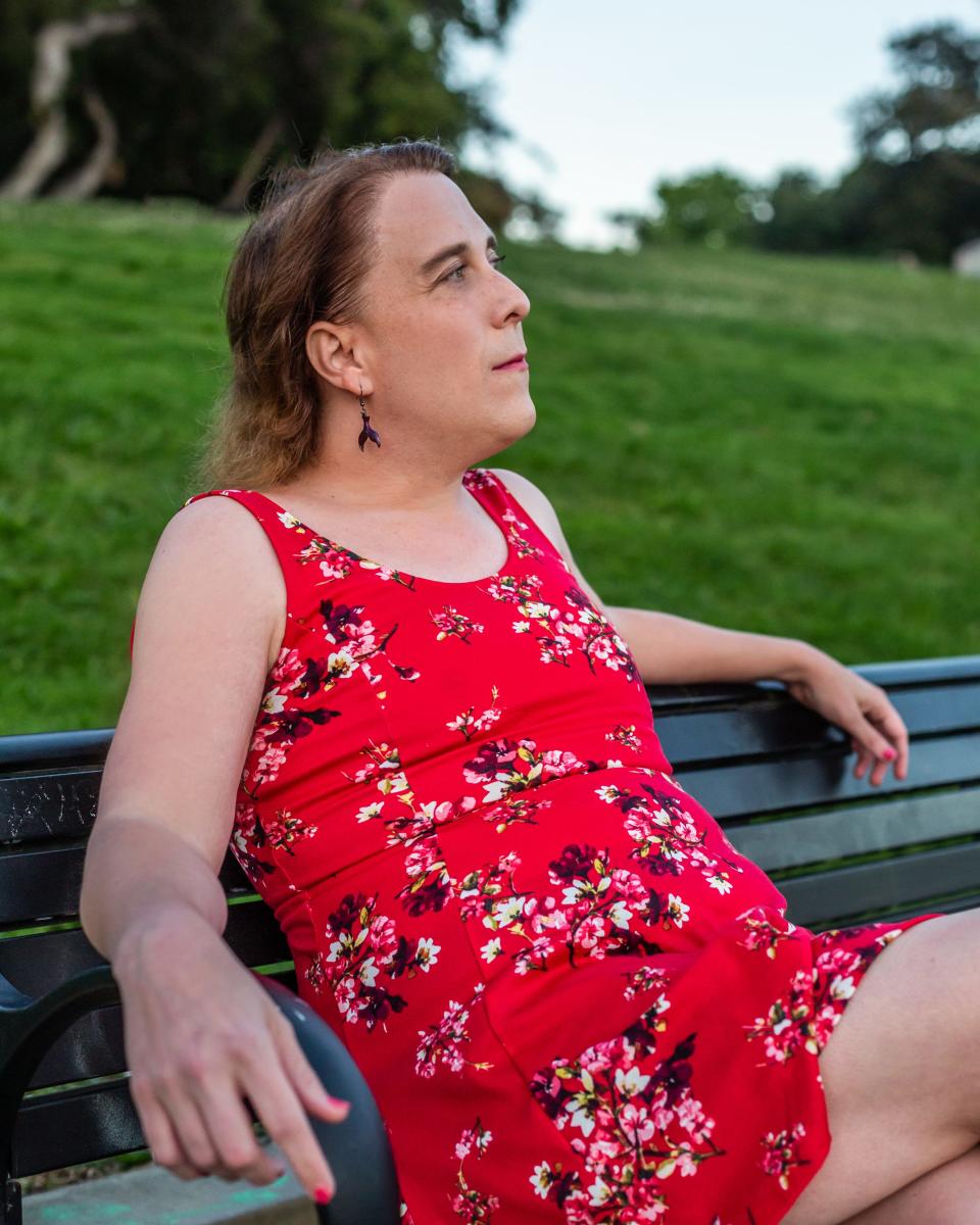 Amy Schneider sits on a bench outside while wearing a red floral dress and drop earrings.