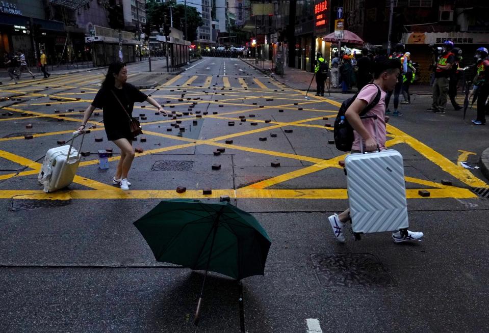 People walk past bricks thrown by protestors after a clash in Hong Kong, Sunday, Oct. 6, 2019. Shouting "Wearing mask is not a crime," tens of thousands of protesters braved the rain Sunday to march in central Hong Kong as a court rejected a second legal attempt to block a mask ban aimed at quashing violence during four months of pro-democracy rallies. (AP Photo/Vincent Yu)