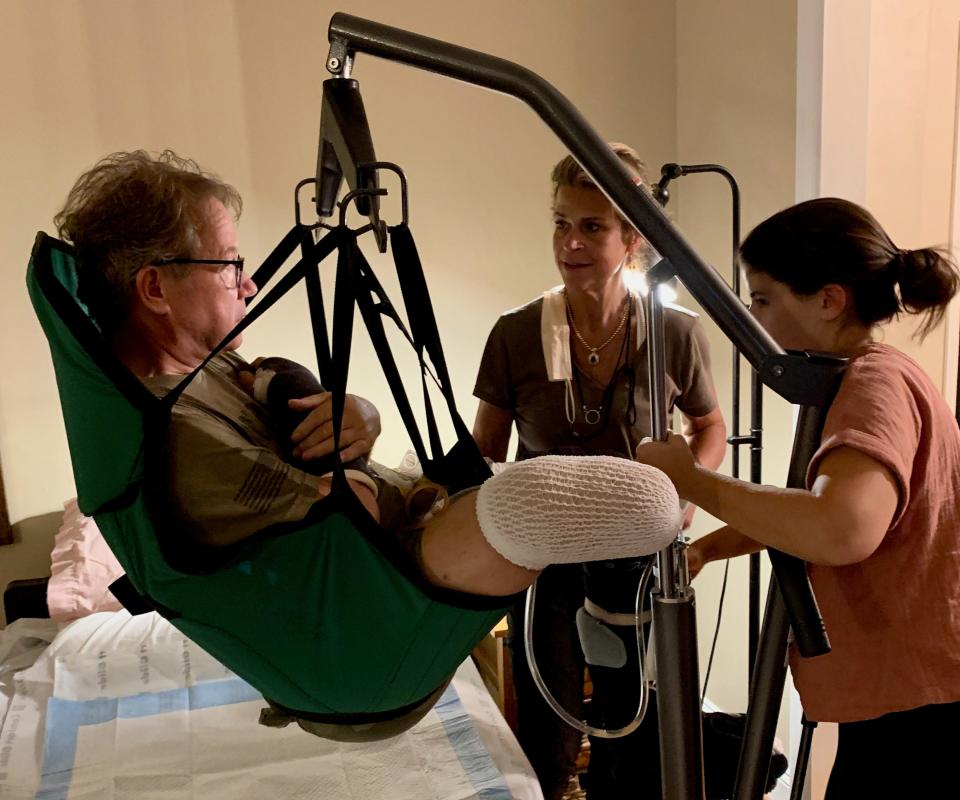 Occupational therapist Brenna Mauro, right; and Laura Spitnale use a Hoyer lift to help Scott Spitnale back into bed shortly after returning home from physical rehab following a June 2021 crash in southern Washington County. This photo was taken in late fall 2021.