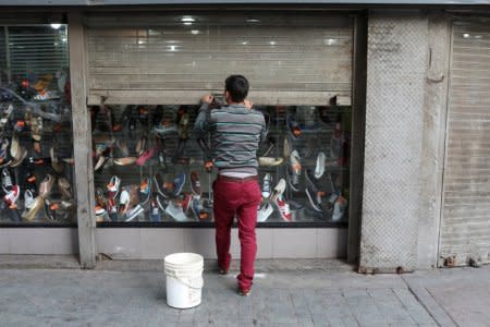 A worker closes the security shutter of a window display at a shoes store in downtown Caracas, Venezuela January 16, 2018. REUTERS/Marco Bello