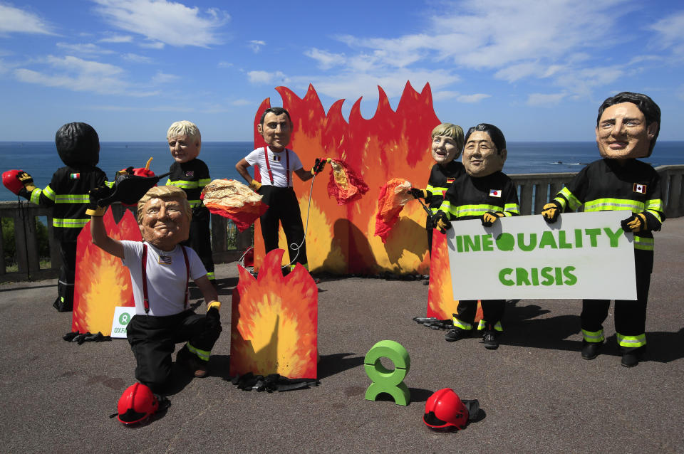 A man wearing a mask President Donald Trump, front left, is joined by other 'world leaders' during a protest ahead of the G-7 summit in Biarritz, France Friday, Aug. 23, 2019. The European Union and Germany are backing French President Emmanuel Macron's call to put the Amazon fires on the agenda of this weekend's G-7 summit of world leaders in France. Other leaders are from left: Italian Premier Giuseppe Conte, Britain's Prime Minister Boris Johnson, French President Emmanuel Macron, German Chancellor Angela Merkel, Japanese Prime Minister Shinzo Abe and Canadian Prime Minister Justin Trudeau. (AP Photo/Peter Dejong)