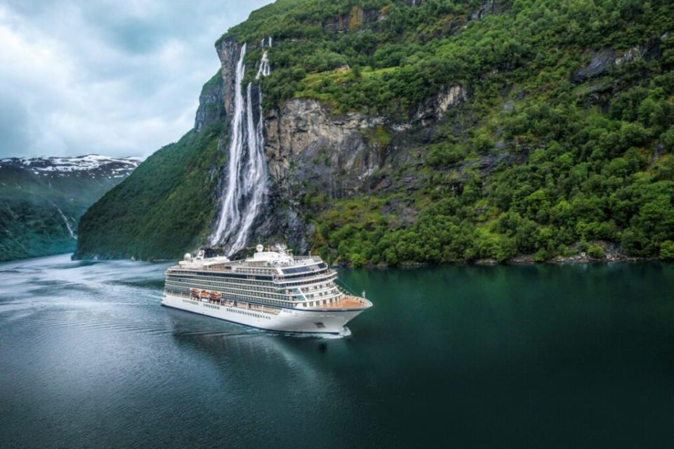 An aerial view of a cruise ship run by Viking Cruises, near Geiranger, Norway, and next to Seven Sisters Waterfall tumbling 1,000 feet into the fjord's water. Source: Viking Holdings Viking