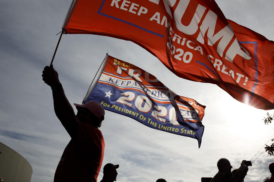 A supporter in a baseball cap waves flags in support of Trump. 