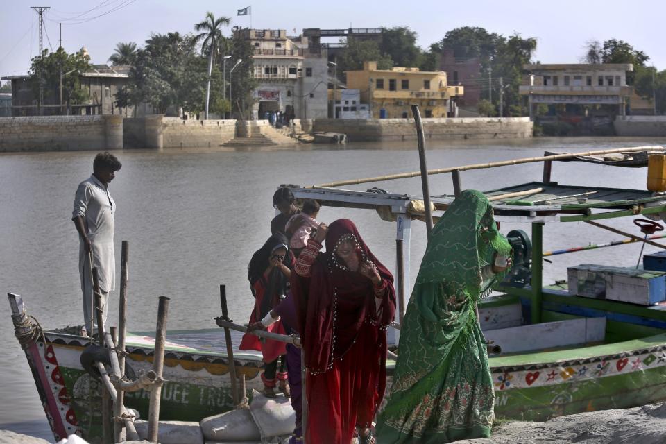 People from Pakistani Hindu community disembark from boat after visiting the Sadhu Bela temple, in background, located in an island on the Indus River, in Sukkur, Pakistan, Wednesday, Oct. 26, 2022. On the banks of the Indus River, which flows through Pakistan and into its southern Sindh province, Hindus wait for brightly colored boats to ferry them to an island that has housed Sadhu Bela temple for almost 200 years. The island was gifted to the Hindu community by wealthy Muslim landlords in Sindh, an unthinkable act in modern-day Pakistan. (AP Photo/Fareed Khan)