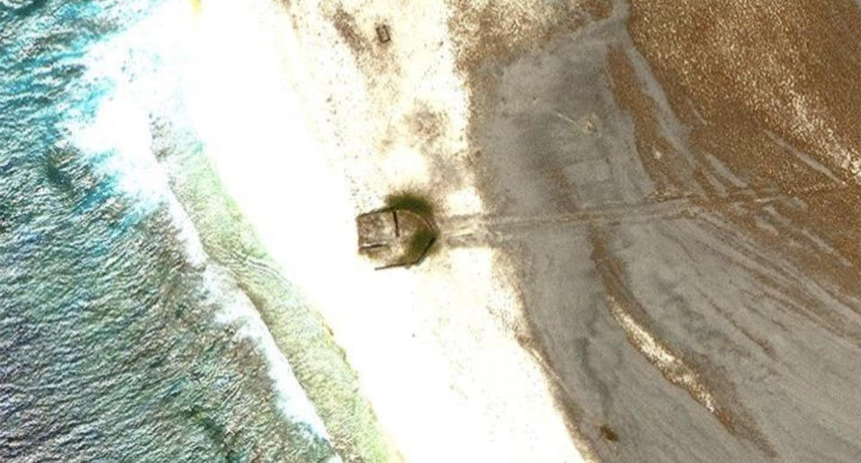A google maps image of a beach showing a brown object that looks like half a boat on the sand with marks that make it look like its been dragged behind it.