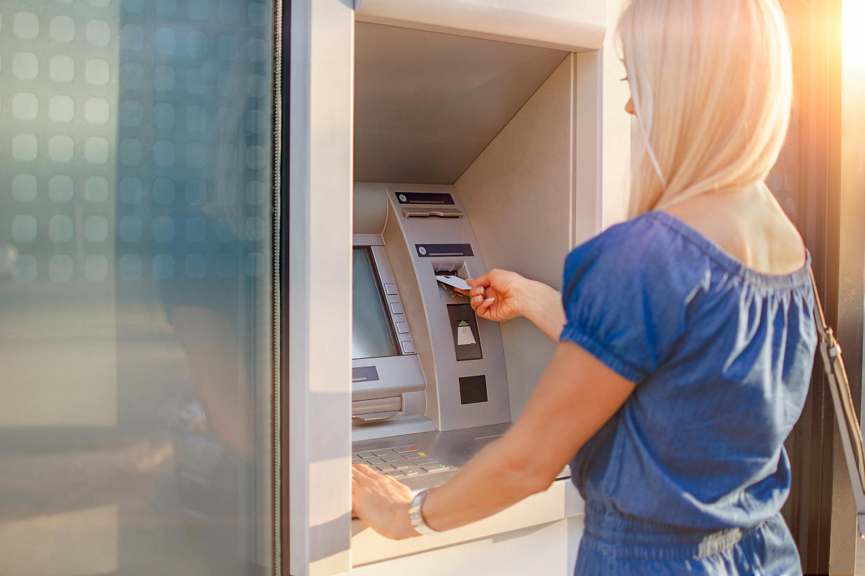 Young blond woman checking account balance, taking money from ATM outdoors