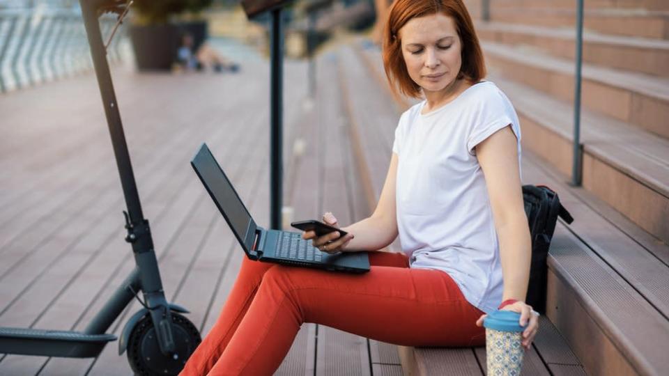 Una mujer sentada en la calle con su laptop desenchufada