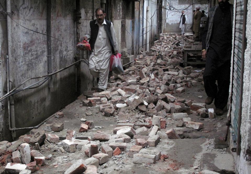 A man with his belongings walks past the rubble of a house after it was damaged by an earthquake in Mingora