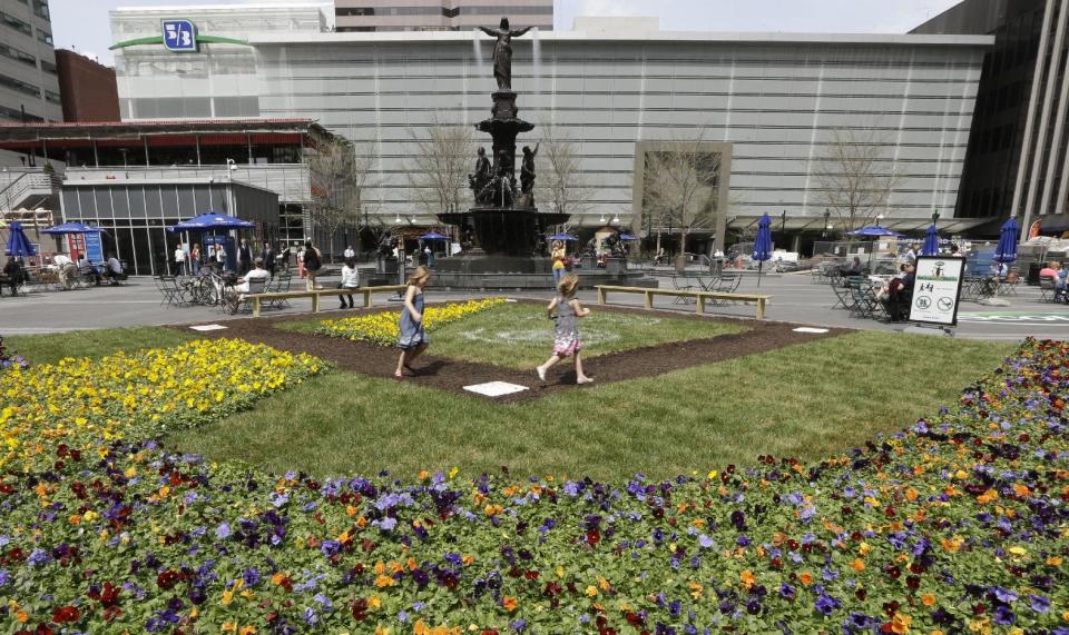 This April 10, 2013 photo shows Hannah Bailey, left, running the bases with sister Eva Bailey on a baseball diamond floral display set up on Fountain Square in Cincinnati. The heart of downtown Cincinnati, Fountain Square underwent a $49 million renovation and reopened in 2006. (AP Photo/Al Behrman)