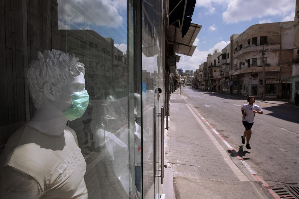 A man runs on an empty street next to a shop offering face masks for sale amid concerns over the country's coronavirus outbreak on Israel's 72nd Independence Day, in Tel Aviv, Israel, Wednesday, April 29, 2020. The Israeli government announced a complete lockdown over their Independence Day to control the country's coronavirus outbreak. (AP Photo/Oded Balilty)