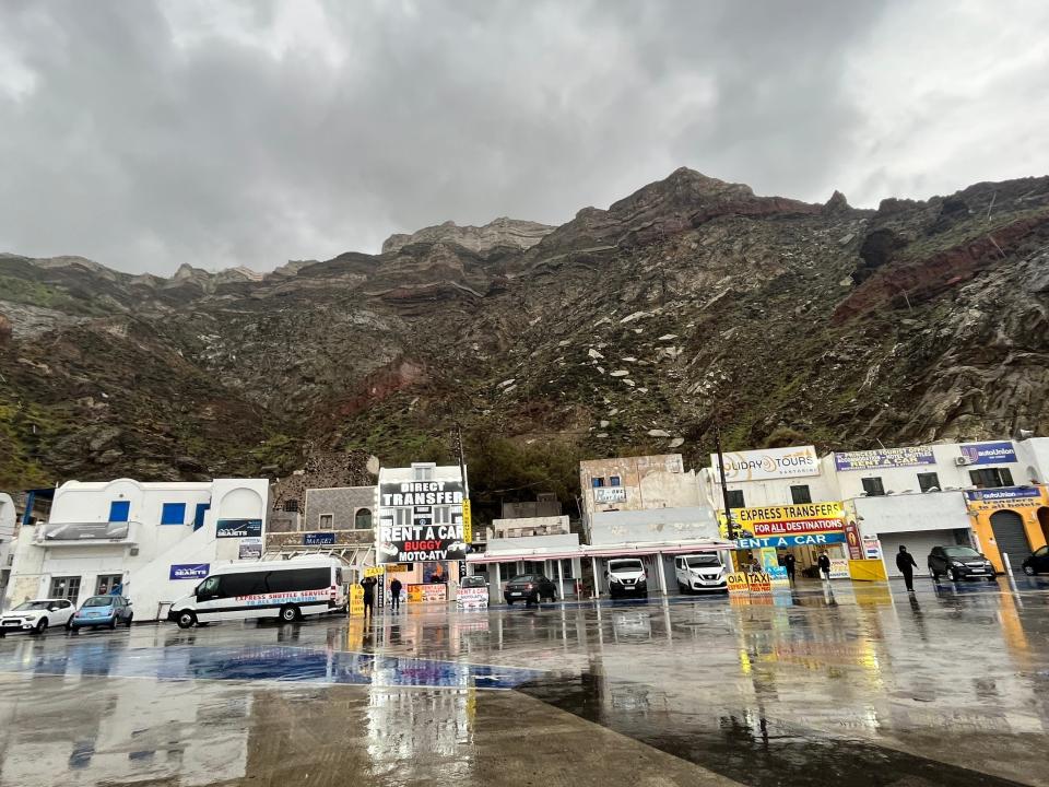 port in Santorini with businesses along a road and mountains behind them