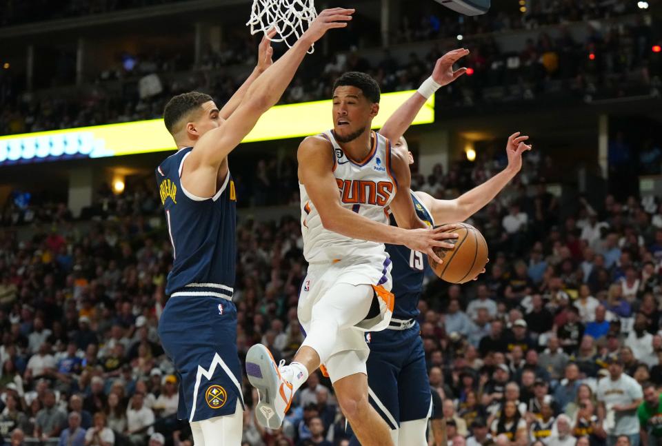 Phoenix Suns guard Devin Booker (1) passes between Denver Nuggets forward Michael Porter Jr. (1) and center Nikola Jokic (15) in the first quarter during game two of the 2023 NBA playoffs at Ball Arena in Denver on May 1, 2023.