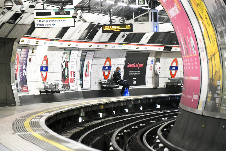 A man wearing a protective face mask to protect against coronavirus, waits for a Central Line underground train on an empty platform at Bank Station, in London, Saturday, April 25, 2020. (AP Photo/Alberto Pezzali)