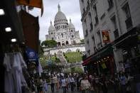 People walk past souvenir shops and restaurants below Sacre Coeur of Montmartre Basilica, ahead of the 2024 Summer Olympics, Monday, July 22, 2024, in Paris, France. (AP Photo/Rebecca Blackwell)