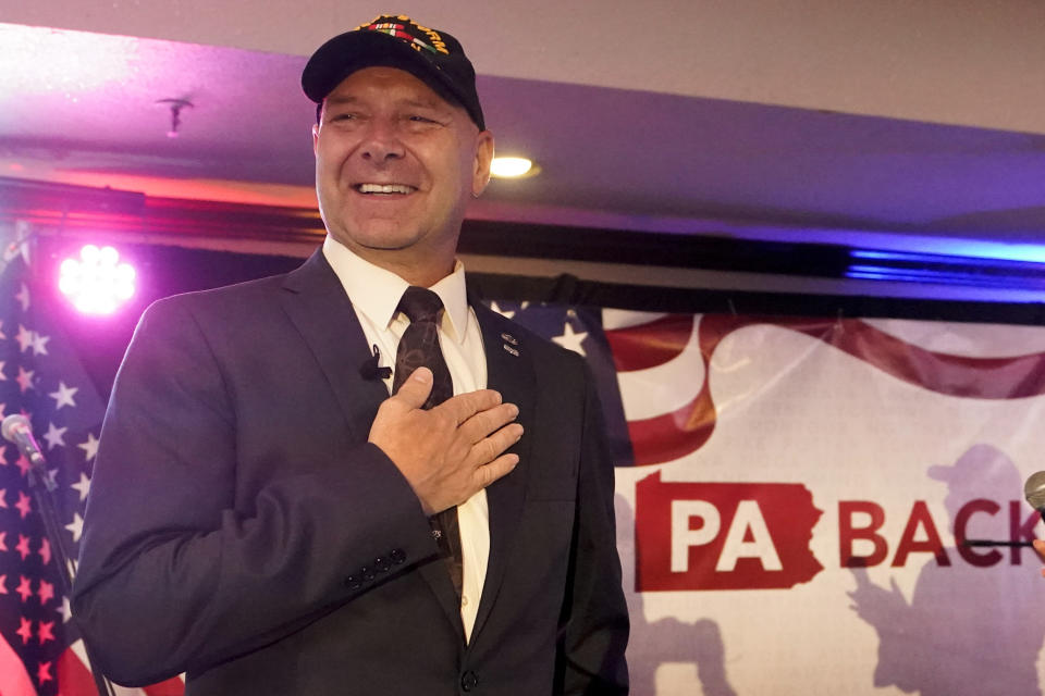 State Sen. Doug Mastriano, in baseball cap, beams as he puts his hand on his heart.