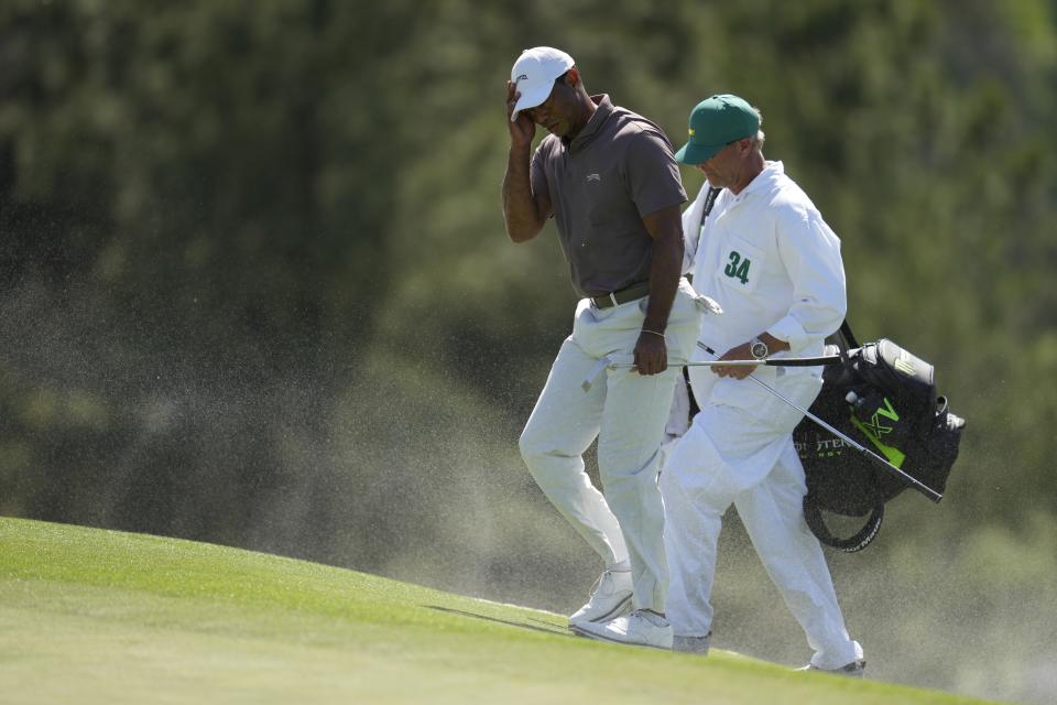 Tiger Woods and caddie Lance Bennett shield, their faces form the blowing sand on the 18th hole during second round at the Masters golf tournament at Augusta National Golf Club Friday, April 12, 2024, in Augusta, Ga. (AP Photo/Ashley Landis)