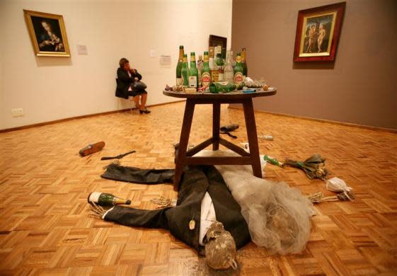 A security guard at the San Carlos museum in Mexico City sits in her chair behind a piece by British artist Damien Hirst titled "Adam and Eve under the table" between two 16th century paintings October 6, 2006.