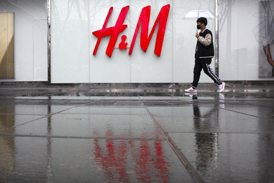 A man carrying an umbrellas walks past an H&M clothing store at a shopping mall in Beijing, Friday, March 26, 2021. H&M disappeared from the internet in China as the government raised pressure on shoe and clothing brands and announced sanctions Friday against British officials in a spiraling fight over complaints of abuses in the Xinjiang region. (AP Photo/Mark Schiefelbein)