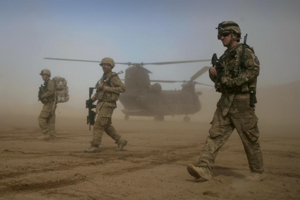 FILE - U.S. soldiers, part of the NATO- led International Security Assistance Force (ISAF), walk as a U.S. Chinook helicopter is seen on the back ground in Shindand, Herat, west of Kabul, Afghanistan, Saturday, Jan. 28, 2012. NATO is set to celebrate on Thursday, April 4, 2024, 75 years of collective defense across Europe and North America as Russia's war on Ukraine enters its third year. (AP Photo/Hoshang Hashimi, File)