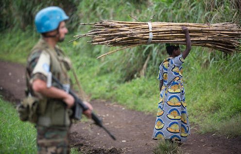 <span class="caption">A UN peacekeeper on patrol as a resident gathers wood in the Beni region of eastern DRC in 2014.</span> <span class="attribution"><a class="link " href="https://dam.media.un.org/CS.aspx?VP3=DamView&VBID=2AM94SK77VV2&PN=1&WS=SearchResults&RW=1440&RH=789" rel="nofollow noopener" target="_blank" data-ylk="slk:UN Photo/Sylvain Liechti;elm:context_link;itc:0;sec:content-canvas">UN Photo/Sylvain Liechti</a></span>