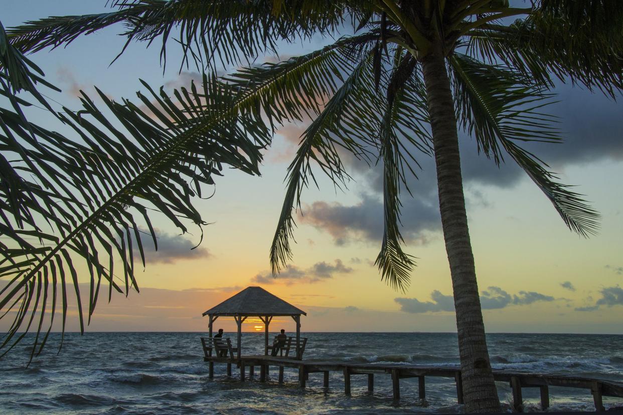 silhouette of two people in the distance watching sunrise from under palapa at end of pier, Placencia, Belize