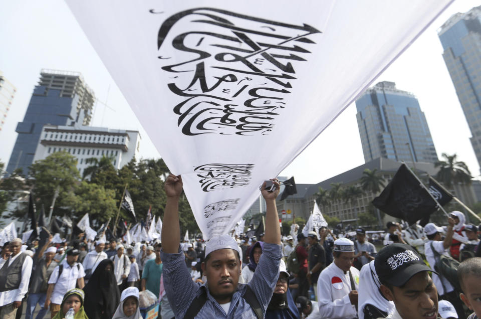 A Muslim man holds a flag with Arabic writings that read: "There's no god but Allah and Muhammad is his messenger" popularly known as "tauhid flag" which is often linked with banned Islamic group Hizbut Tahir Indonesia, during a protest in Jakarta, Indonesia, Friday, Nov. 2, 2018. Thousands of conservative Muslims staged the protest in the capital against the burning of the flag by members of Nahdlatul Ulama, the country's largest mainstream religious organization. (AP Photo/Achmad Ibrahim)