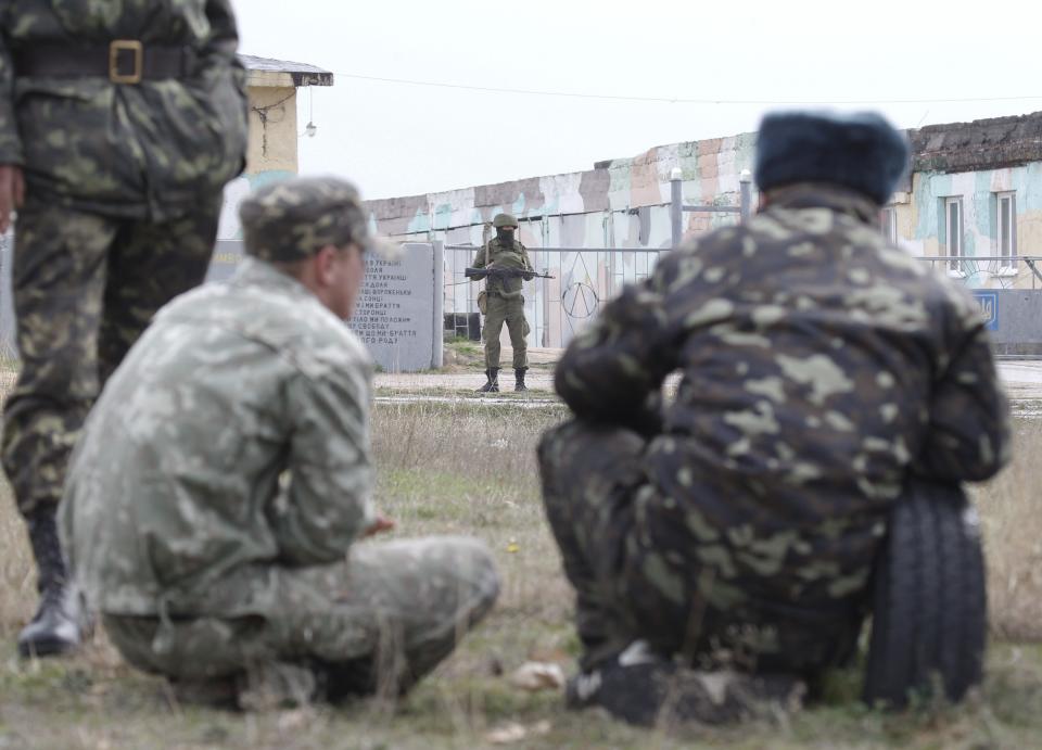 Ukrainian servicemen look at a Russian serviceman as they wait at the Belbek airport in the Crimea region