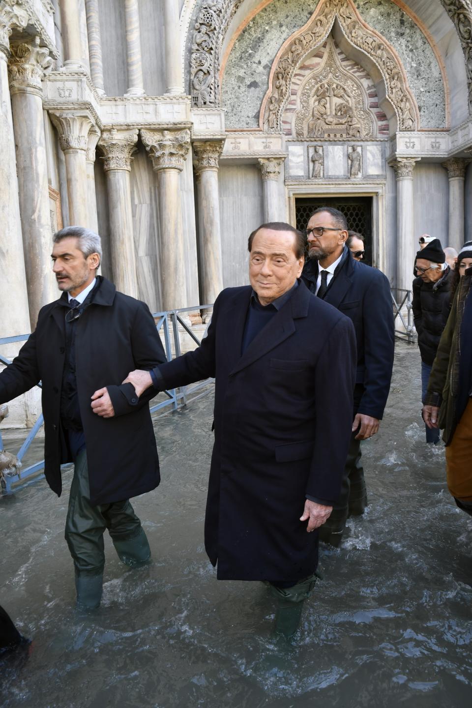 Former Italian Premier Silvio Berlusconi wades through water in St. Mark's Square inVenice, Italy, Thursday, Nov. 14, 2019. The worst flooding in Venice in more than 50 years prompted calls to better protect the historic city from rising sea levels as officials calculated hundreds of millions of euros in damage. (AP Photo/Luigi Costantini)