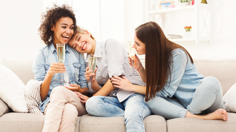 Happy female friends chatting and drinking wine at home.