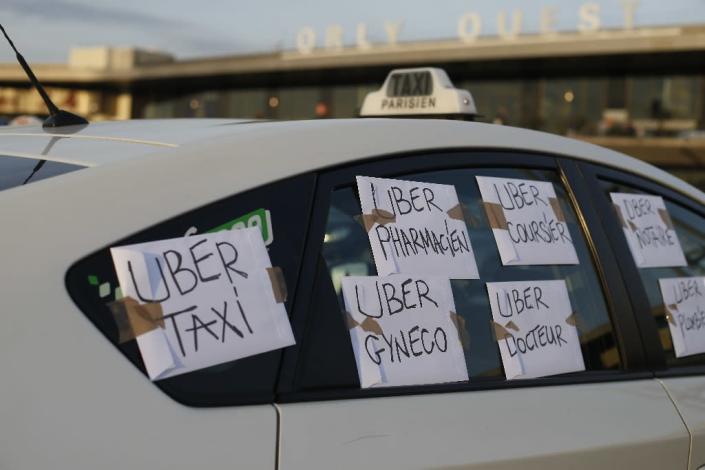 A taxi with signs reading "Uber taxi, Uber pharmacist, Uber doctor..." is parked outside Orly Airport, south of Paris, on June 25, 2015, as hundreds of taxi drivers demonstrate against taxi app UberPOP (AFP Photo/Thomas Samson)