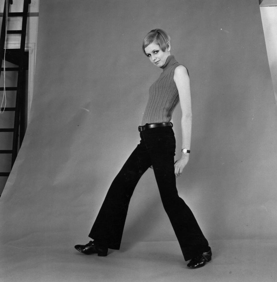 Twiggy models flared trousers and a sleeveless top in a photographer's studio.