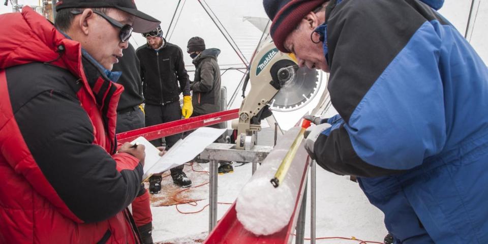 Two men wearing winter gear look at an ice core in a mobile laboratory.