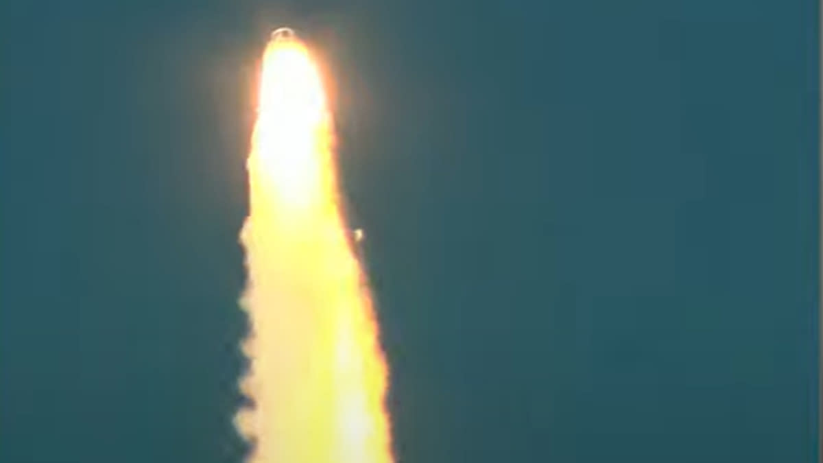  A space capsule launches away from its rocket atop a pillar of flame, with blue sky in the background. 