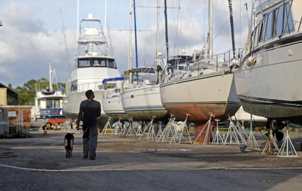 Manuel Arias walks with a guard dog, Toto, past boats that were dry-docked inland in preparation for Tropical Storm Gordon, expected to make landfall as a hurricane later in the evening, in Pass Christian, Miss., Tuesday, Sept. 4, 2018. (AP Photo/Gerald Herbert)