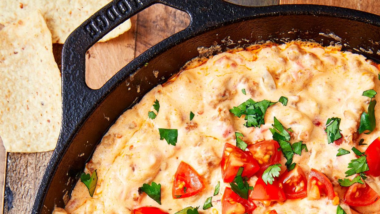 closeup of sausage dip in a cast iron pan garnished with cilantro and chopped tomatoes