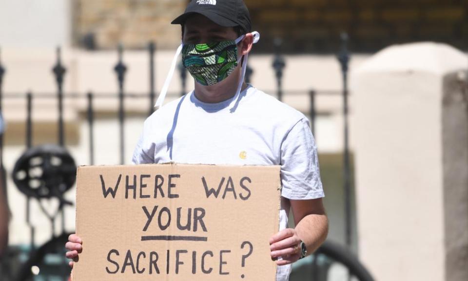 A masked protester outside Dominic Cummings’s home holding a placard saying 'Where was your sacrifice?'