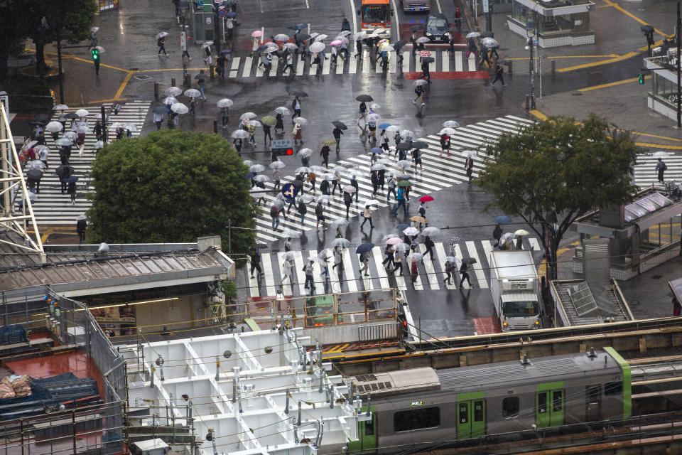 Commuters with umbrellas walk a crosswalk as Typhoon Mindulle travels off the coast of Japan Friday, Oct. 1, 2021, in Tokyo. (AP Photo/Kiichiro Sato)