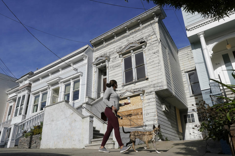 A pedestrian walks a dog past a recently sold Victorian home in San Francisco, Friday, Jan. 14, 2022. The decaying, 122-year-old Victorian marketed as "the worst house on the best block" of San Francisco recently sold for nearly $2 million — an eye-catching price that the realtor said was the outcome of overbidding in an auction. (AP Photo/Jeff Chiu)