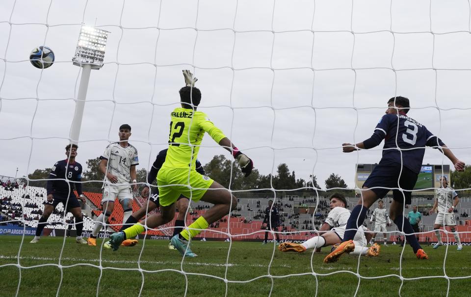 Italy's Cesare Casadei, on the ground, right, scores against Dominican Republic's goalkeeper Xavier Valdez, during a FIFA U-20 World Cup Group D soccer match at the Malvinas Argentinas stadium in Mendoza, Argentina, Saturday, May 27, 2023. (AP Photo/Natacha Pisarenko)