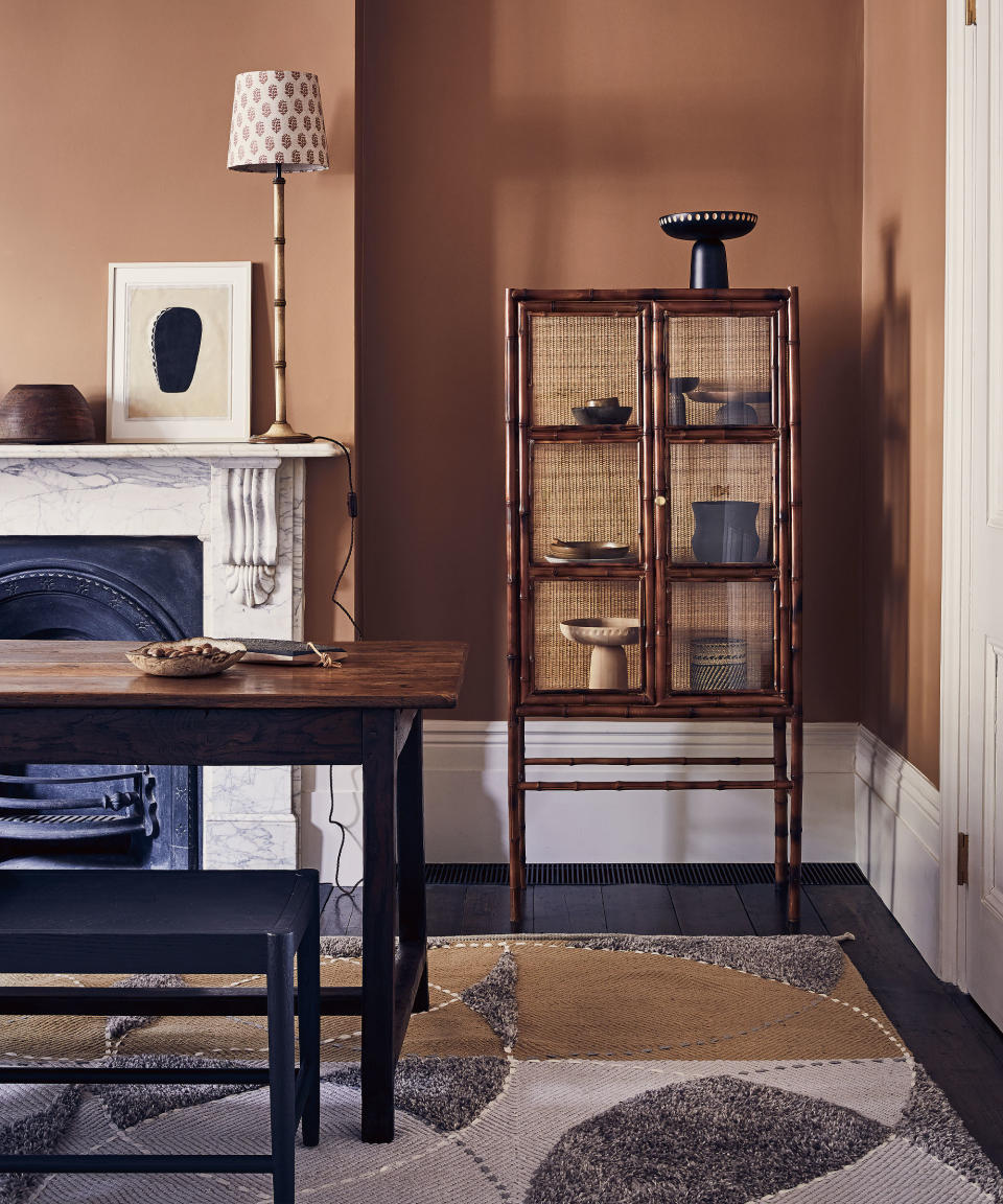 Dining room with black wooden flooring, brown walls, white coving and skirting board and dark wooden furniture on a grey, yellow and white rug