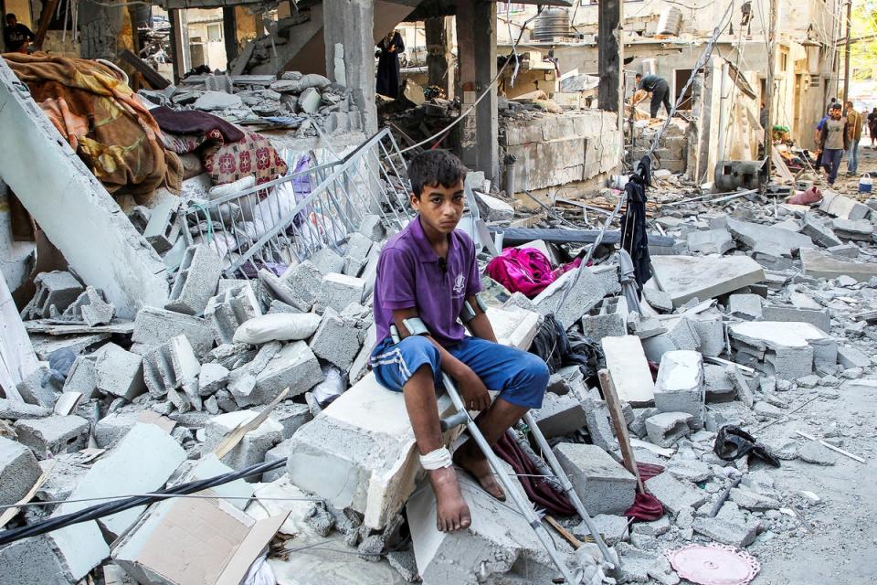 A wounded Palestinian sits on debris at the site of an Israeli strike on a house in Rafah (Reuters)